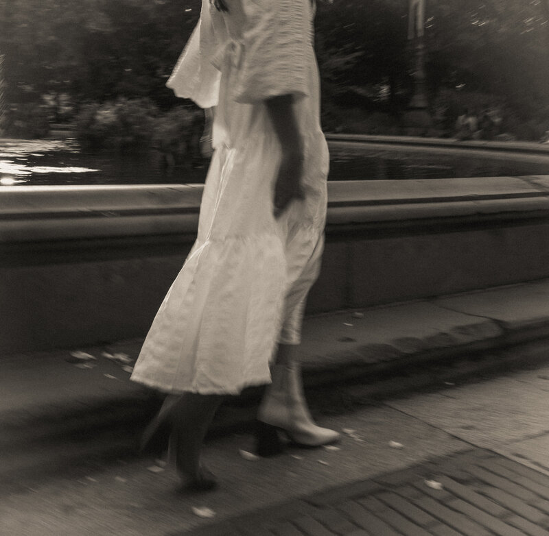 Black and white image of a woman in a summery dress and boots walking