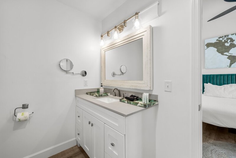White bathroom vanity with double sinks and large mirror, tropical accessories, and peek into king suite at Tropical House.