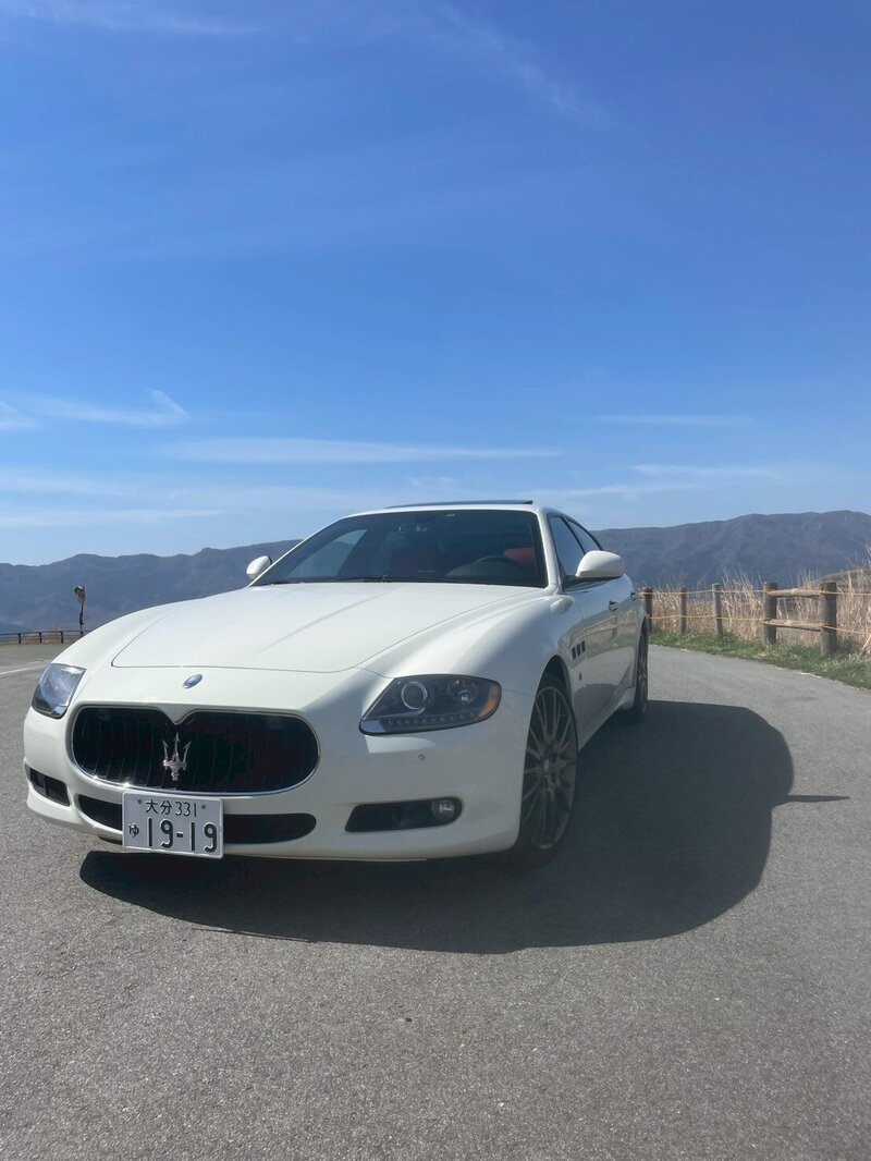 Rear view of a white Maserati driving along an open mountain road under a clear blue sky, evoking a sense of freedom and adventure.