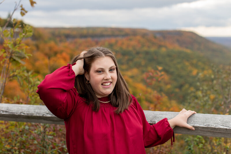 Senior stands in front of fall foliage
