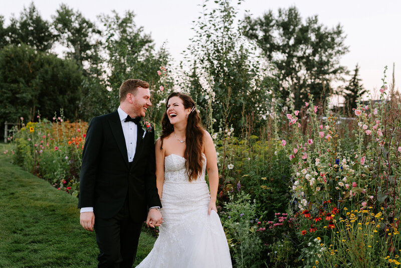 A bride and groom walk through the wildflowers at The Gathered near Calgary, Alberta