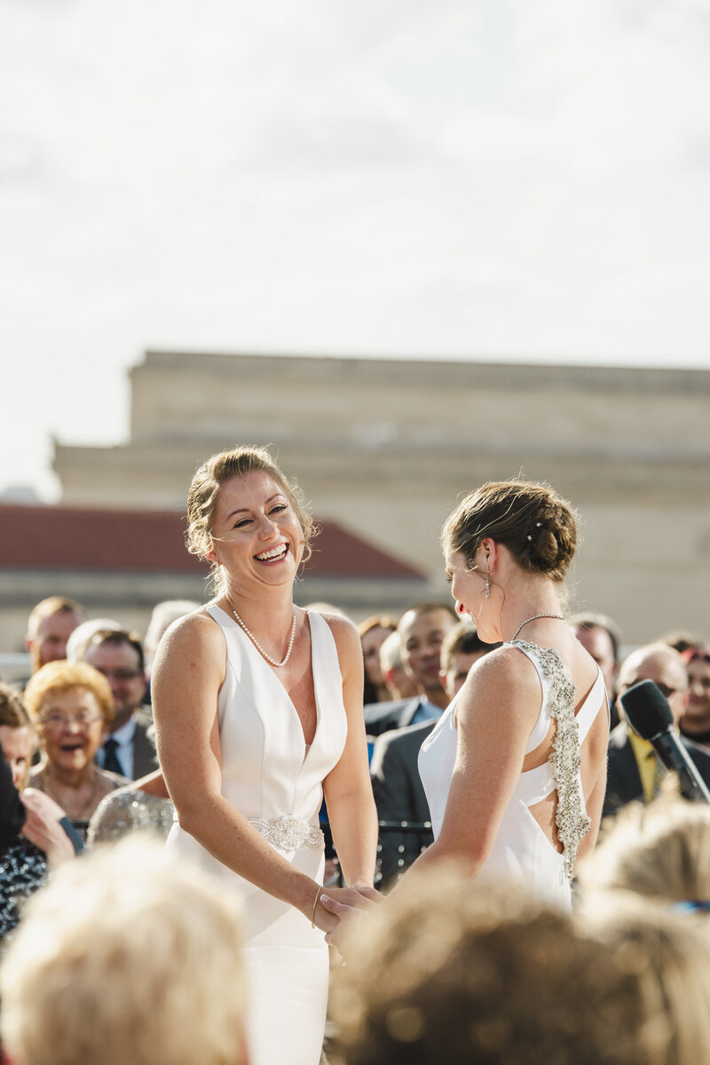 Two brides holding hands and laughing during their wedding ceremony
