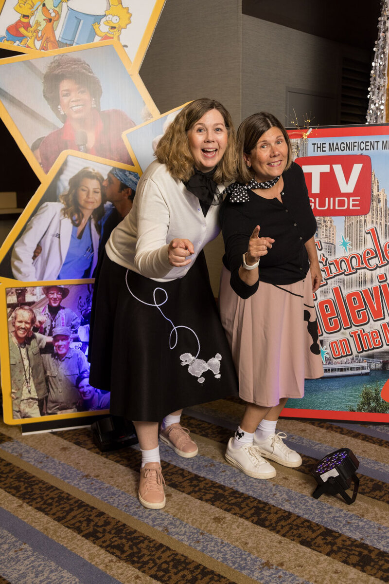 Two women standing in front of a tv guide sign