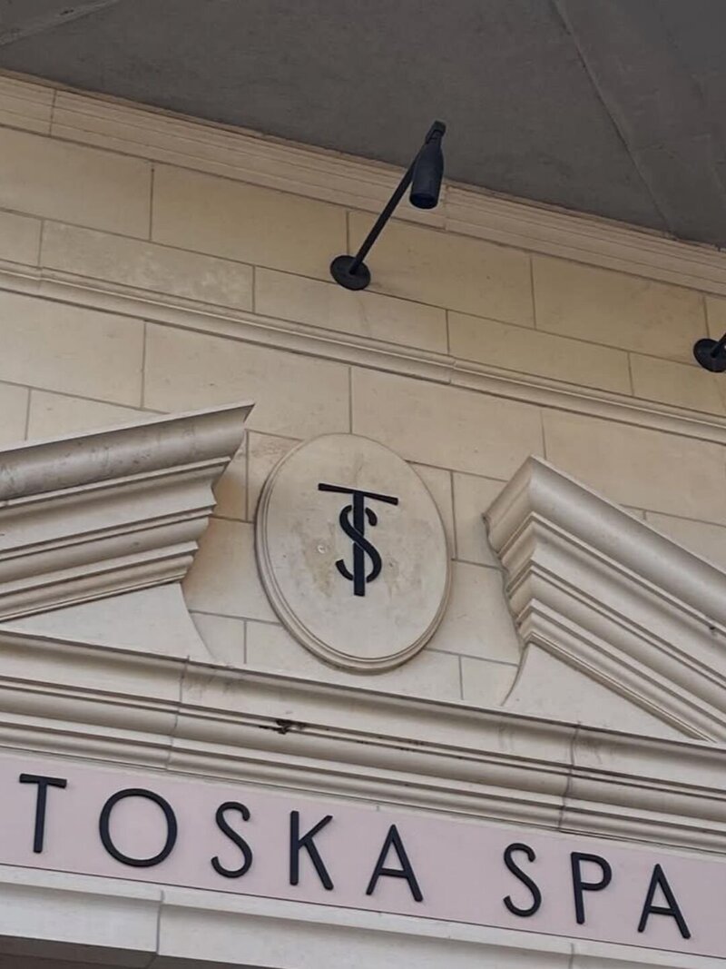 Classic black Toska Spa sign with monogram mounted on stone wall at exterior entrance