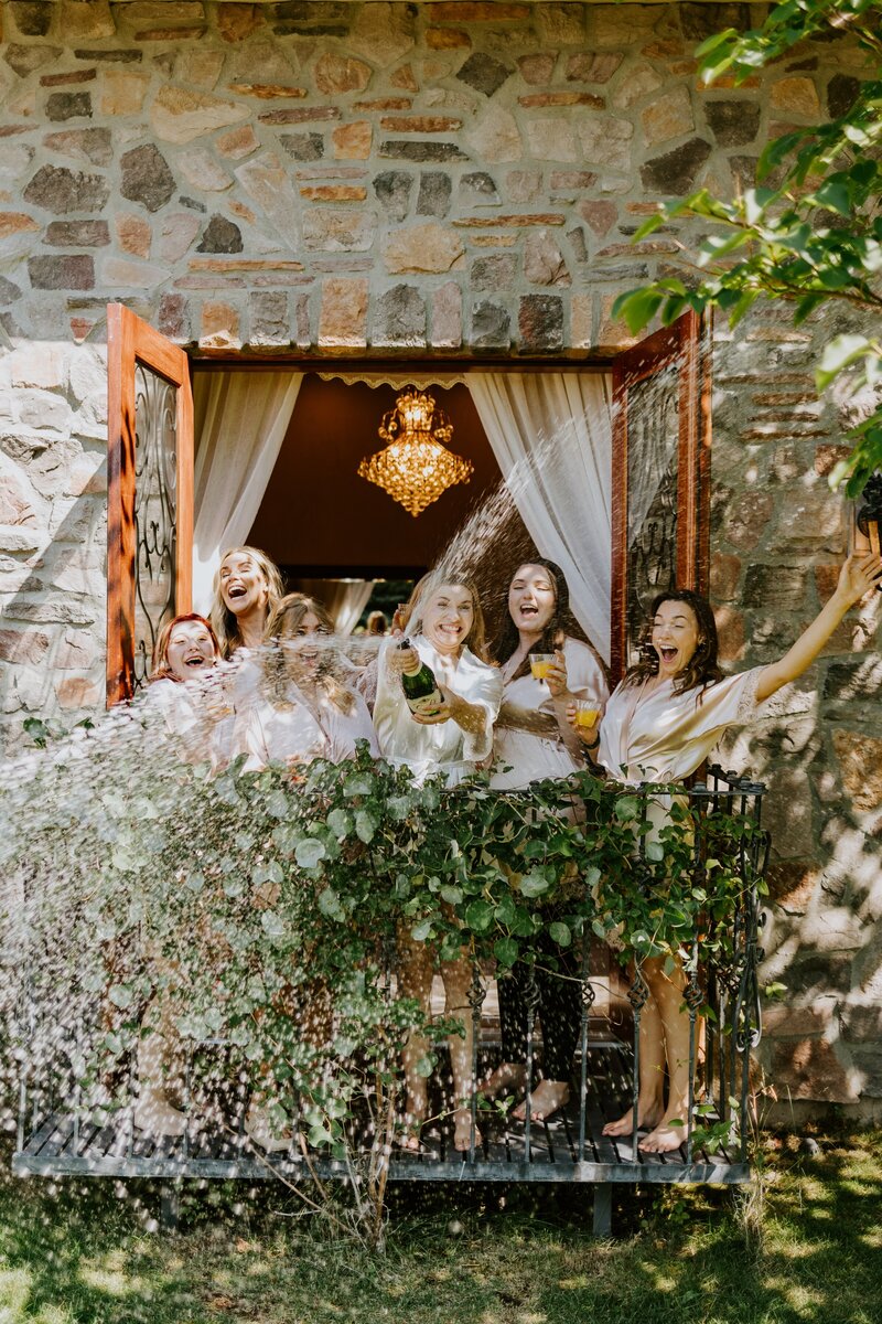 Bridal party pops a bottle of champagne at their chateau event center wedding.