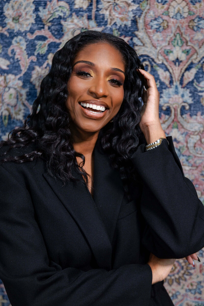 Shaniece Jones smiling wearing a black blazer with her hand by her head.