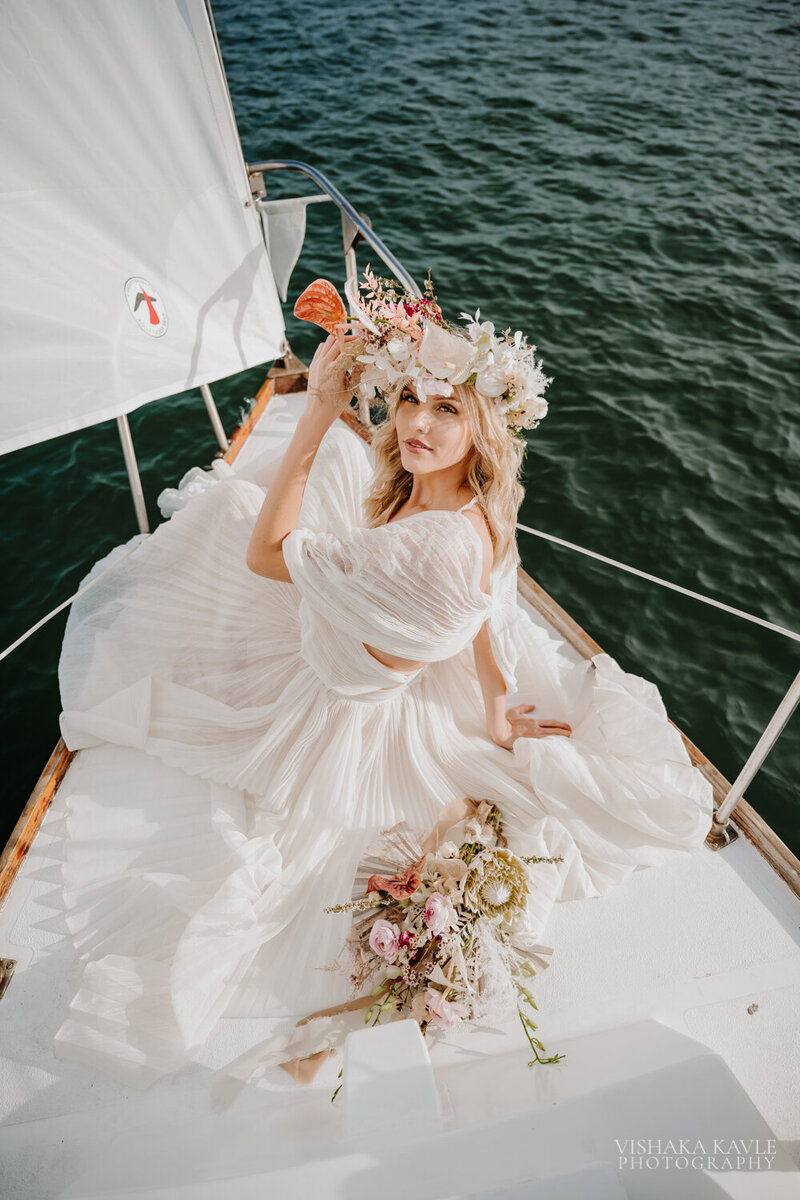 bride wearing her bridal gown and holding bridal bouquet while sitting on a boat in the water