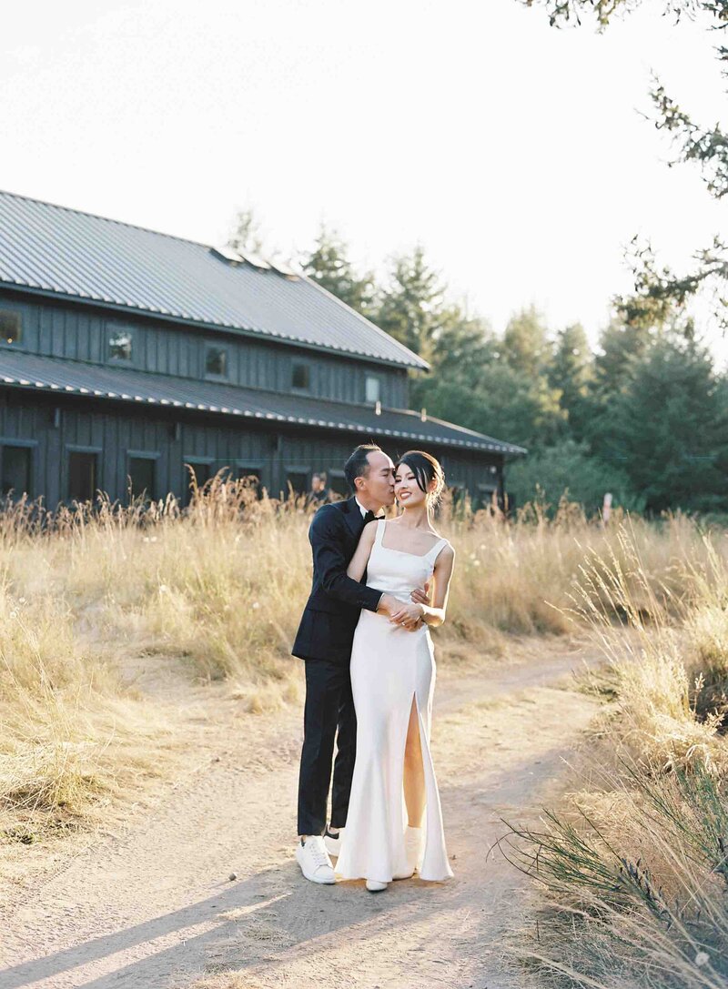 Bride and groom hugging each other in field of tan grass at sunset