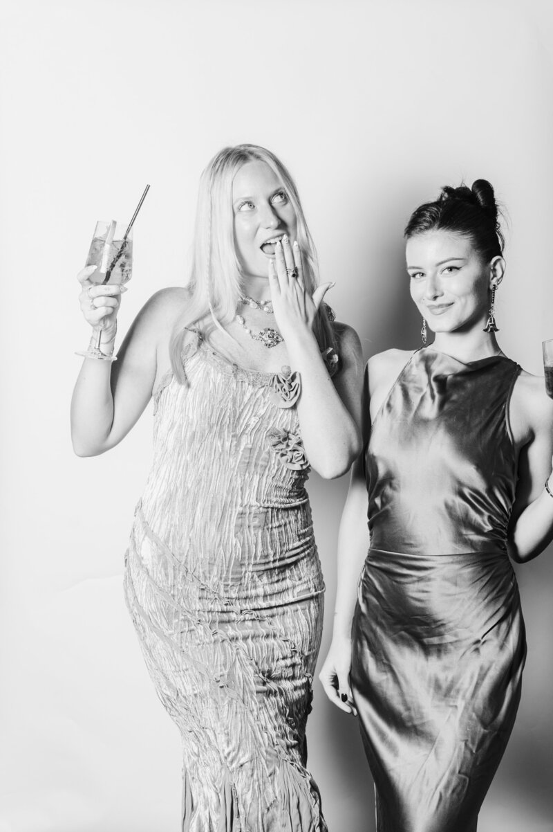 Playful black and white portrait of two women holding cocktails and posing at a Vogue Portrait photo booth in Richmond, VA.