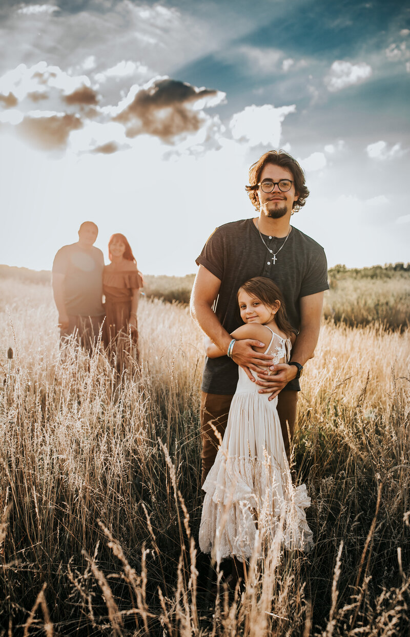 siblings standing on the field, parents standing behind  them, golden hour, sunset, field in Toledo