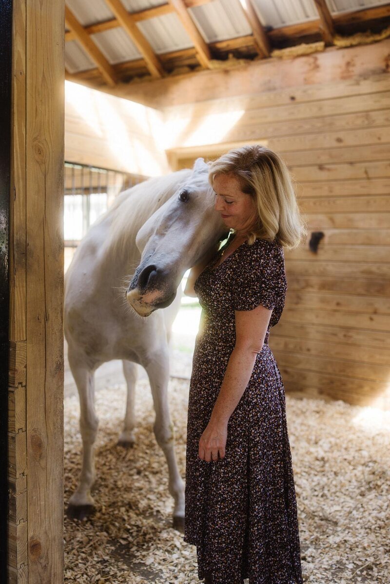 Leiko standing in quiet connection with her horse inside the barn at Peace Horse Collective, inviting visitors to reach out and begin their equine-assisted healing journey in the Berkshires