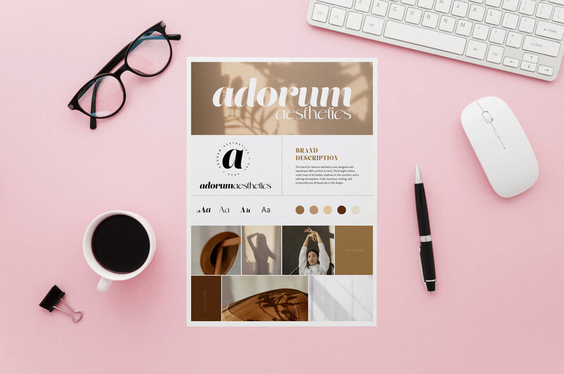 Modern brand design on a piece of paper on a pink desk surrounded by glasses, coffee, and various desk items.