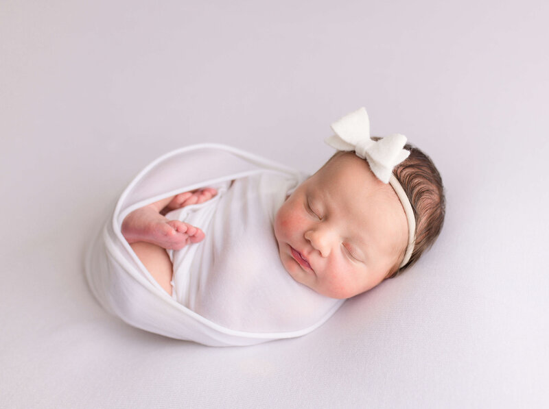 infant swaddled in white with white bow