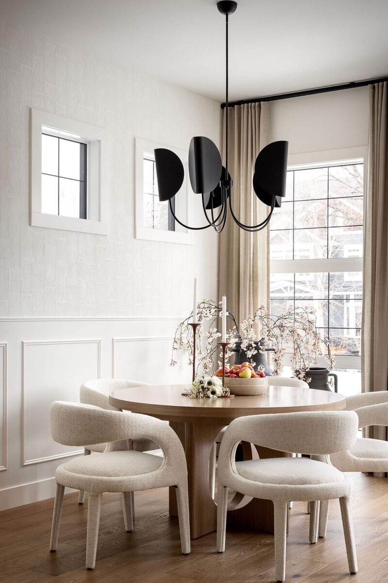 Minimalist dining space featuring a round table, black accents, and airy lighting that balance function with warmth and style.
