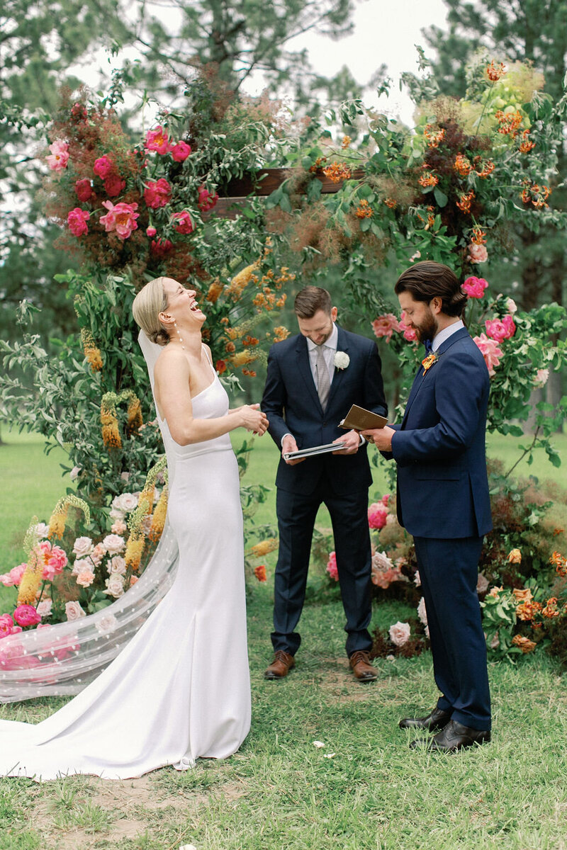 Kelly and Joe standing at their floral altar during their outdoor wedding ceremony in Bend, Oregon, with a vibrant arbor and garden-style aisle flowers by Summer Robbins Flowers