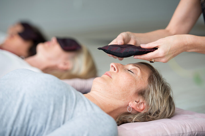 An eye pillow being placed onto the eyes of a woman laying down