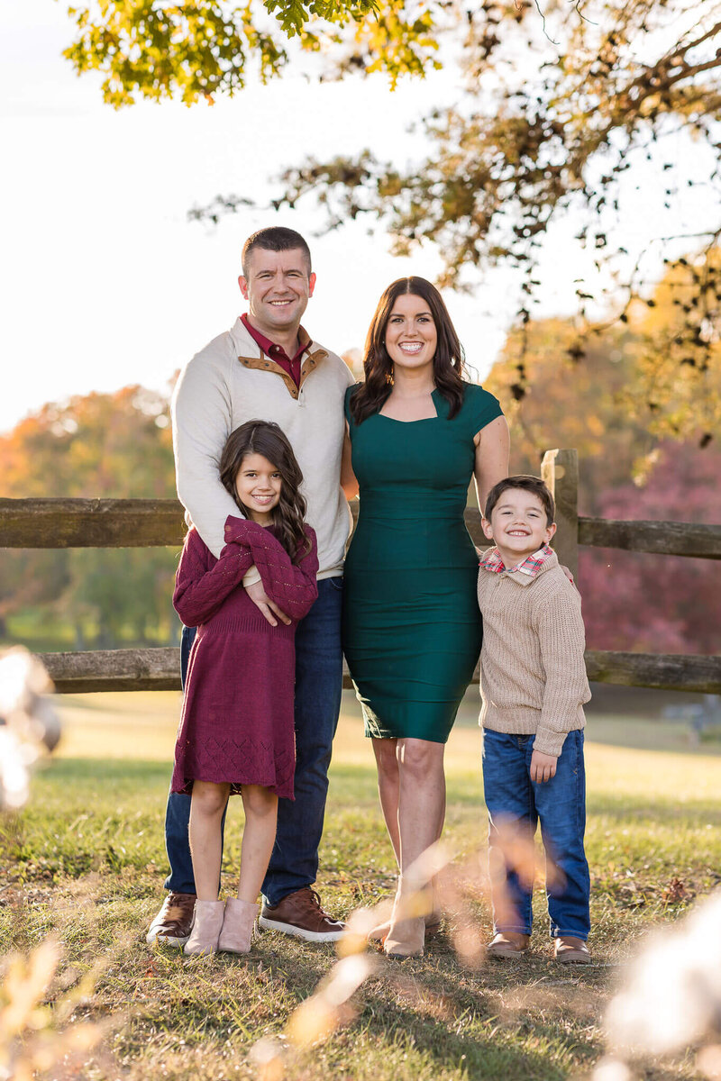 A family of four standing up against a fence and smiling at the camera at Burke Lake Park.