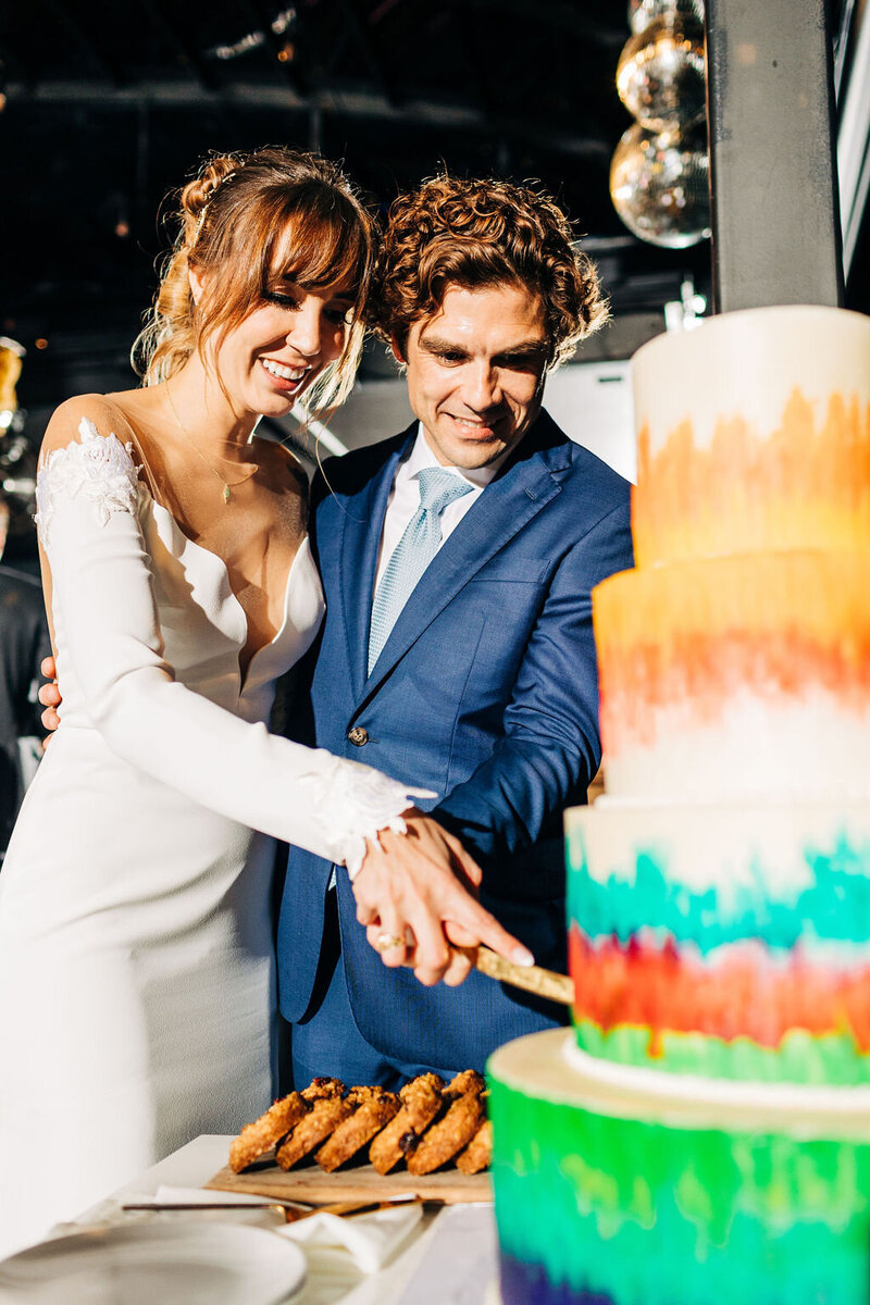 Bride and groom cutting a colorful tiered wedding cake during their Austin reception, planned with personality and vibrant flair.
