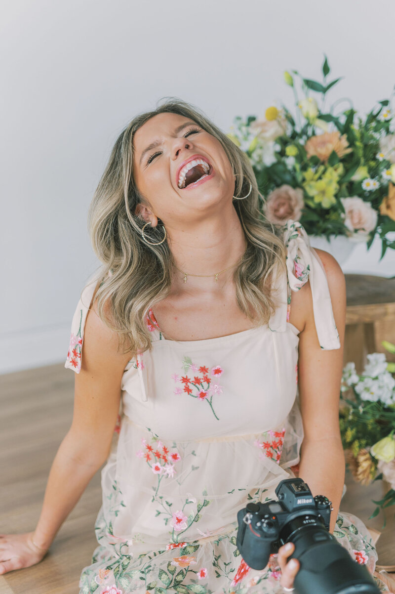 Headshot of Lindsey Kristian in a floral dress laughing with her head tilted back