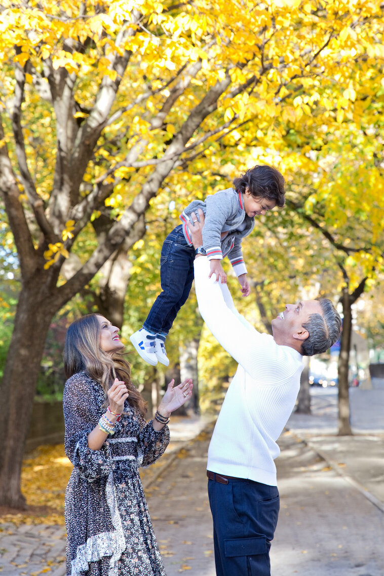 dad holds little boy up in the air as mom looks on during family photo shoot in NYC