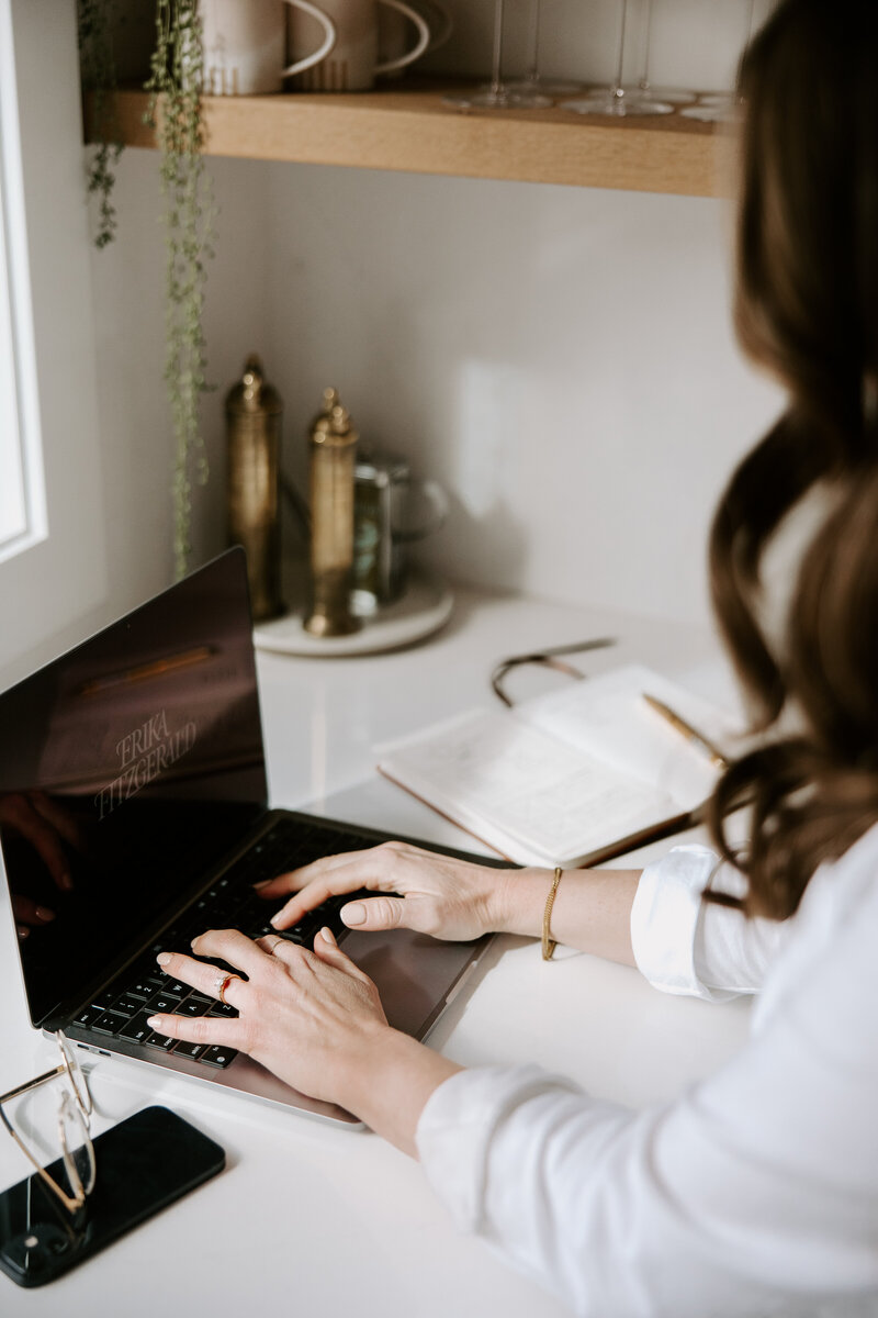 SEO website copywriter Erika Fitzgerald typing on a laptop with an open journal filled with website copywriting and strategy notes