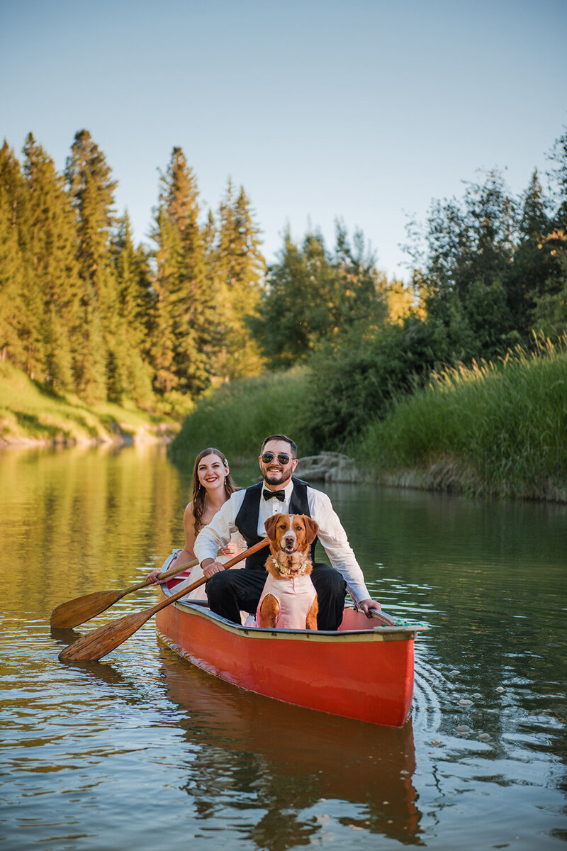 A bride and groom paddle a canoe with their dog on their wedding day in Montana.