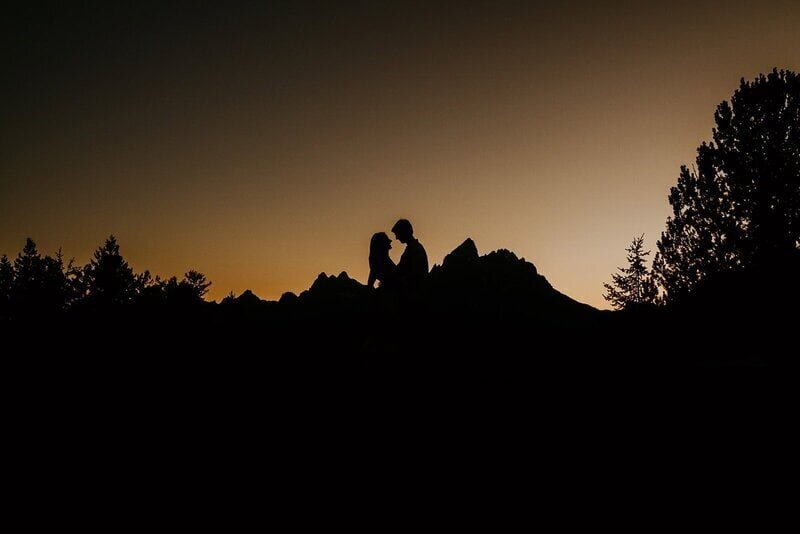 man and woman are seen in a silhouette with the grand tetons behind them