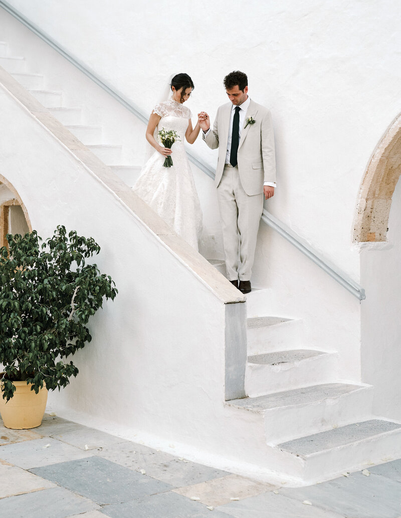 bride and groom walking down white  stairs in greece