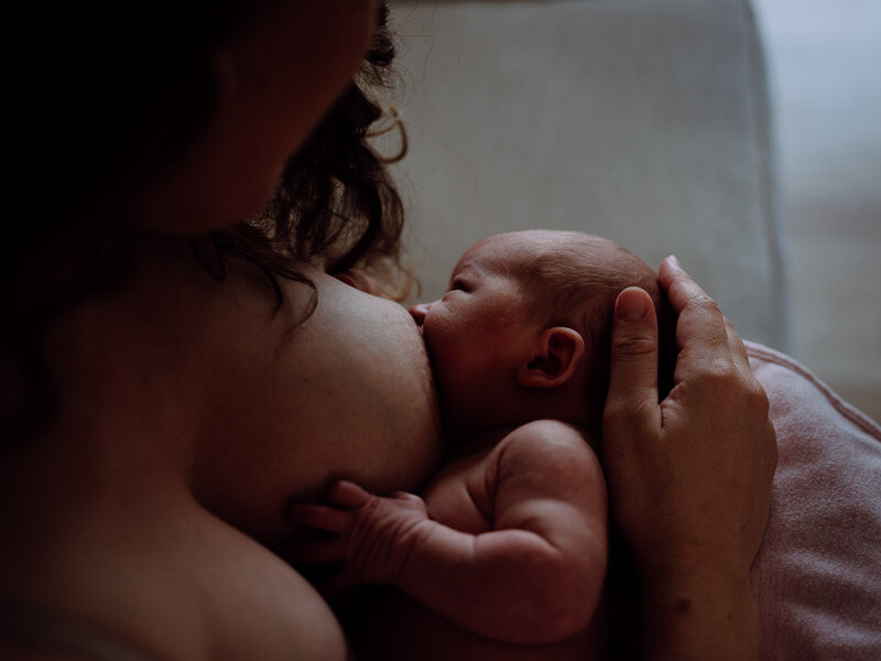 Mother breastfeeds her newborn baby skin to skin.