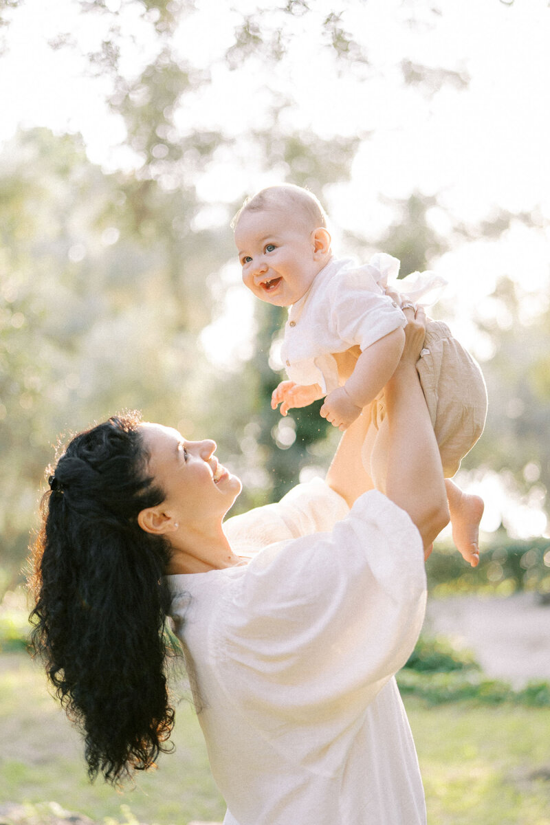 Happy mom holding her smiling baby in sunlight, captured during emotional family photoshoot in Toronto