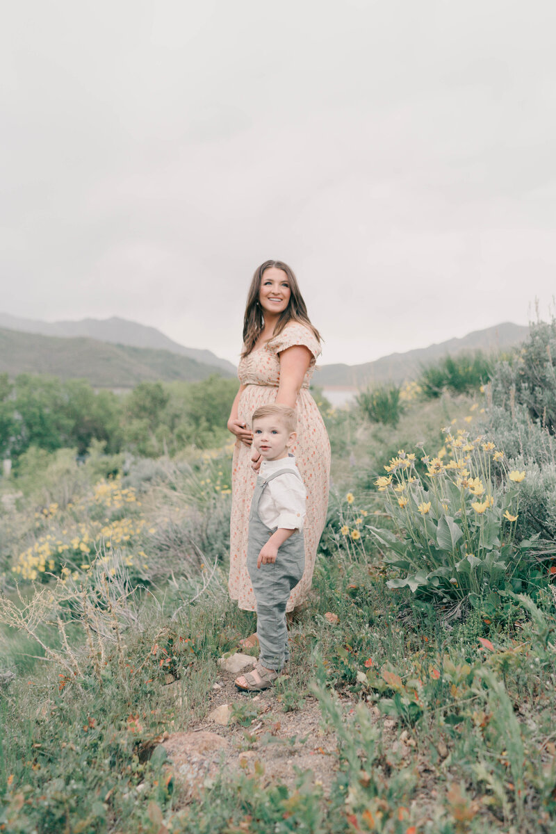 Elegant mom in white gown framed by mountain peaks and soft skies. CAPTURED BY Newborn Photography Salt Lake City, Newborn Photographer Riverton, Maternity Photographer Salt Lake City.