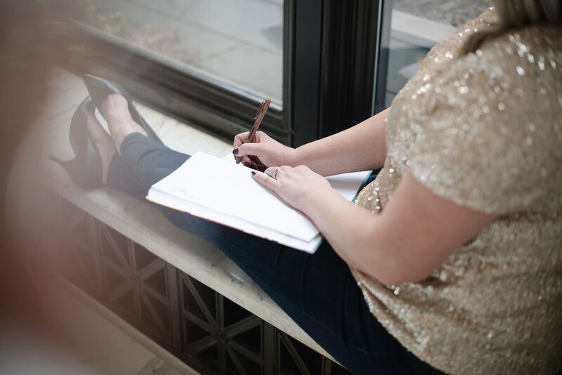 Woman in gold sparkly blouse writes in her notebook in a windowsill