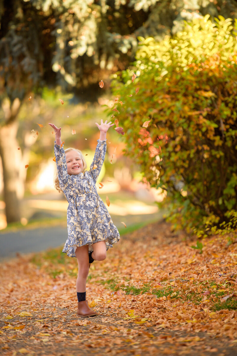 little girl in a white dress stomping through a flowering orchard with her arms swinging during photography with boise photographer Tiffany Hix in Boise Idaho