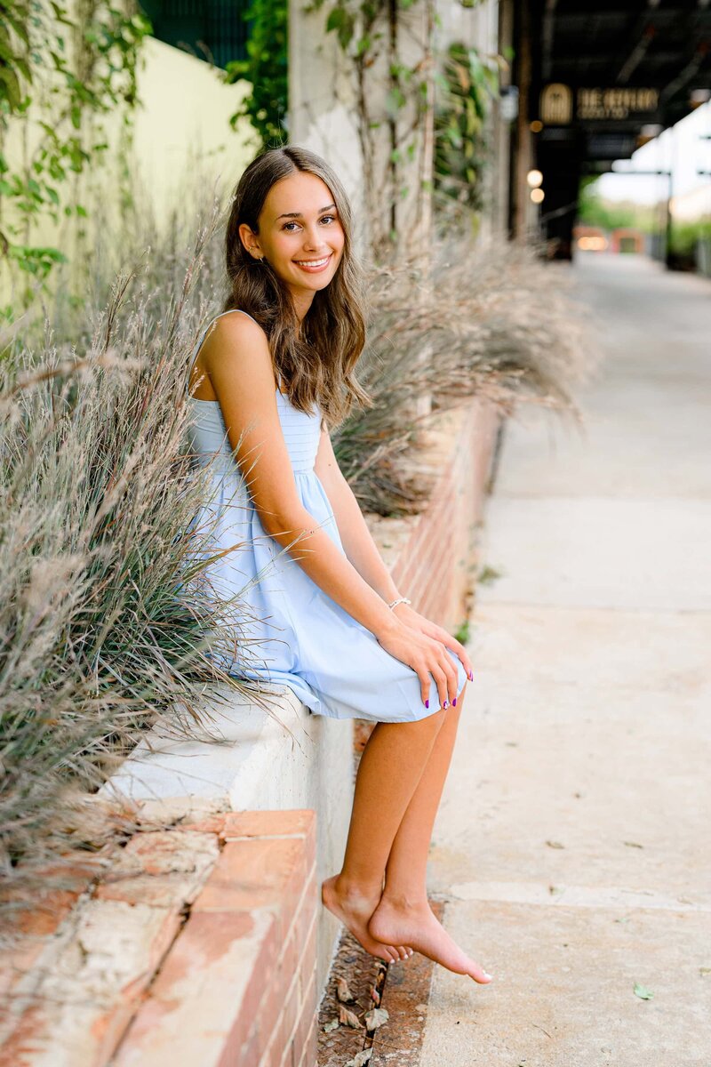 senior sits on wall in blue dress