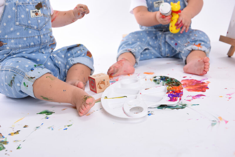 Close-up of twin toddlers’ feet and hands covered in colorful paint during a messy and fun toddler art-themed photo shoot.