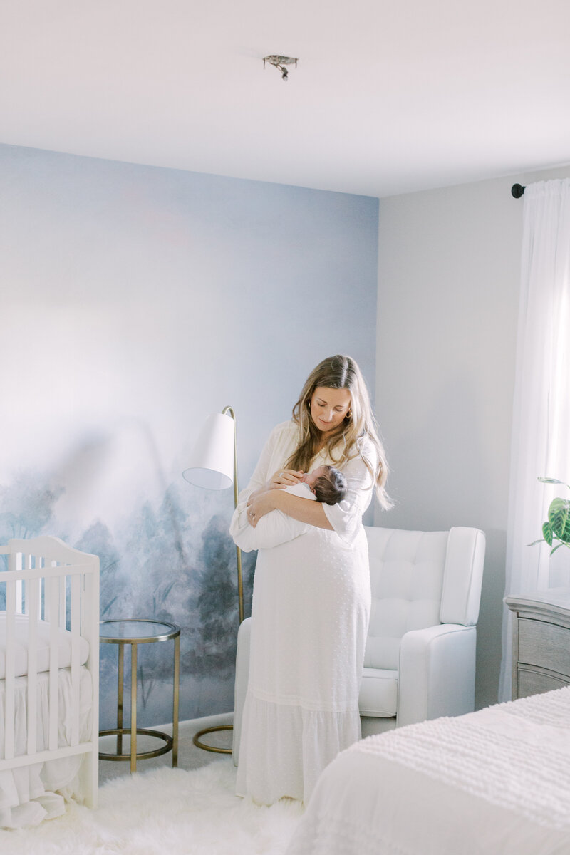 Mother holding newborn son in blue and white nursery with Angelique Jasmin Photography