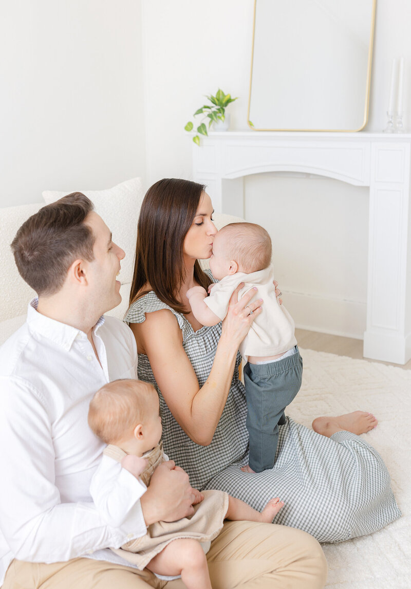 mom kisses baby boy and dad smiles while holding baby girl