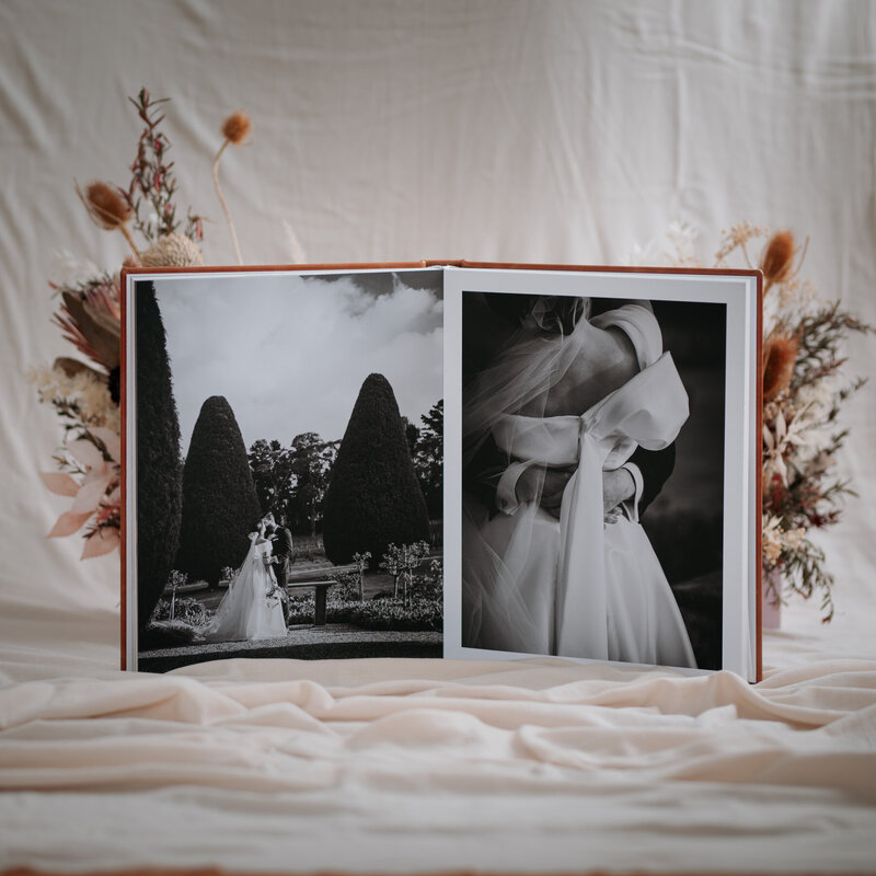 Wedding album open to spread of bride and groom in a garden on the left and a close up of the brides dress on the right.