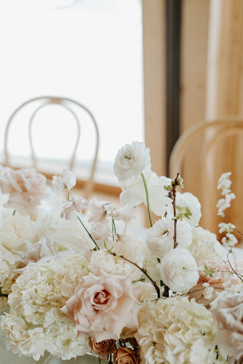 Close-up of reception table with white hydrangea, neutral roses, and bleached fern in lucite vases, styled with candlelight at Jenay and Daniel’s wedding by Summer Robbins Flowers in Central Oregon
