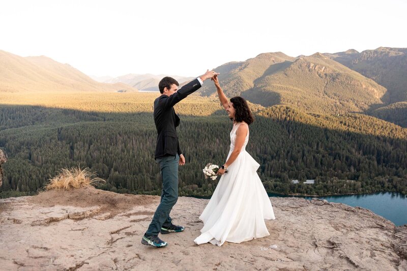 A couple dancing in wedding clothings on a cliff overlooking a lake