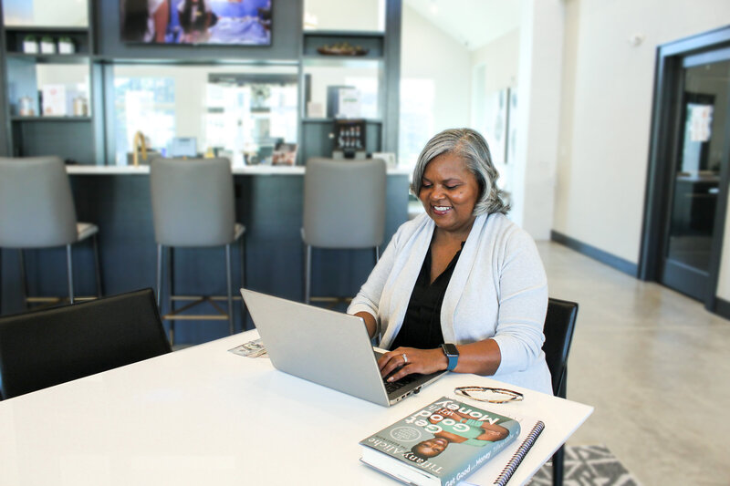 Angela typing on her laptop at a table with finance books and money on it