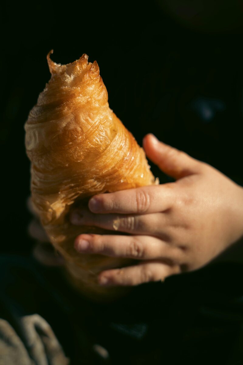 little toddler hands holding a croissant in a café or coffee shop