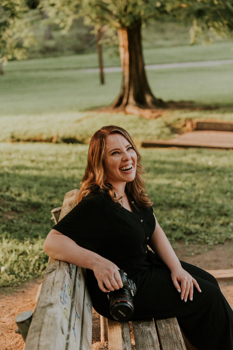wedding photographer sitting on bench holding camera and laughing