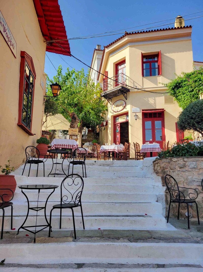 Sunlit café with red shutters and checkered tablecloths in the Plaka neighborhood of Athens ©Stephanie Dosch | theViatrix Curated Greece Travel Planning