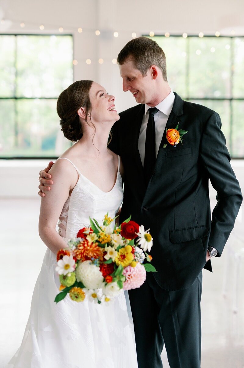 bride and groom gaze at each other happily on wedding day in minneapolis while bride holds colorful bouquet