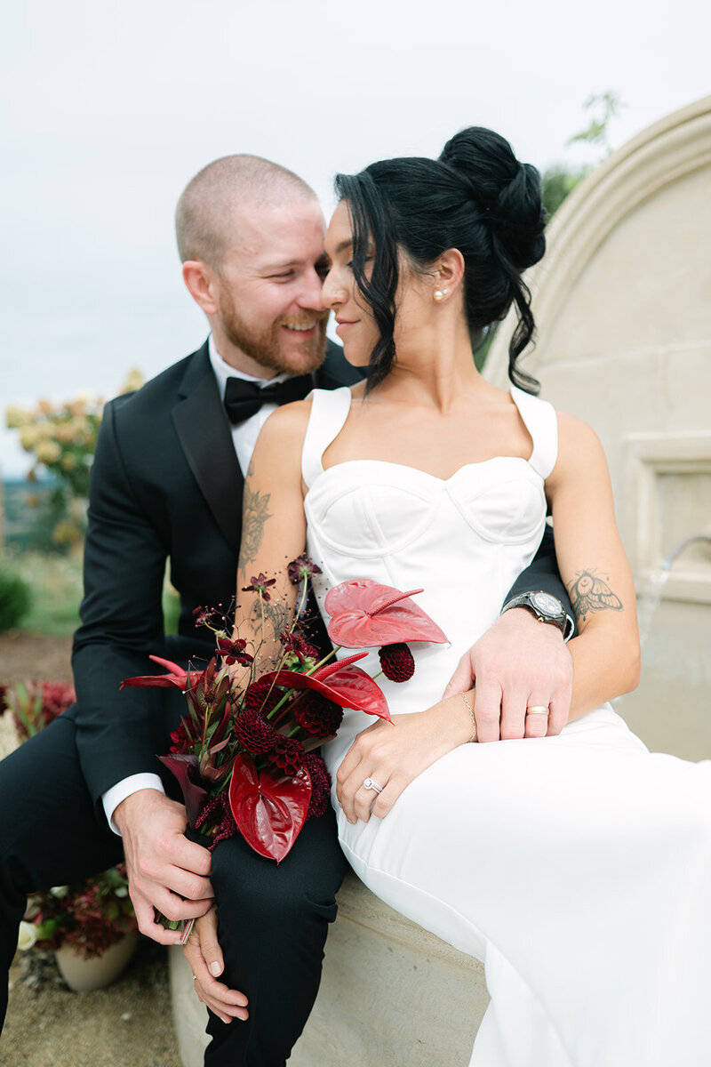 bride in white dress pose with groom holding red bouquet