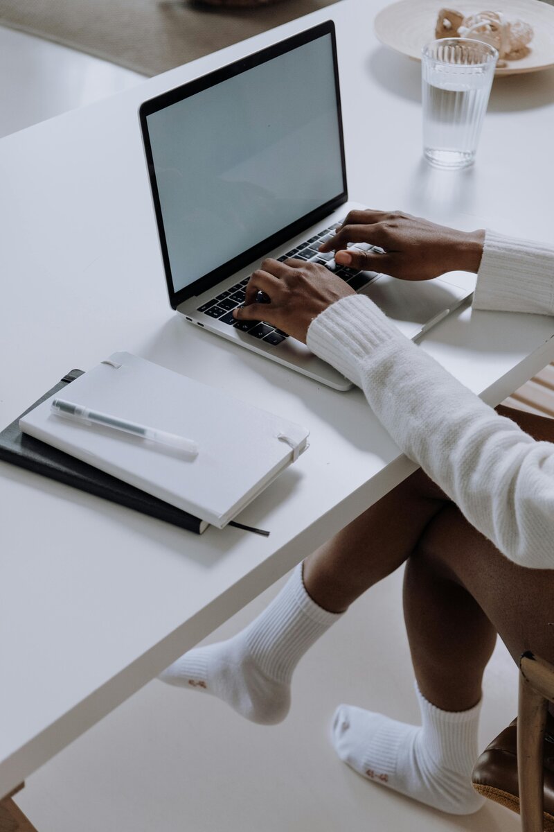 Top down view of a woman with ripped jeans who is working on a laptop, surrounded by books and a planner