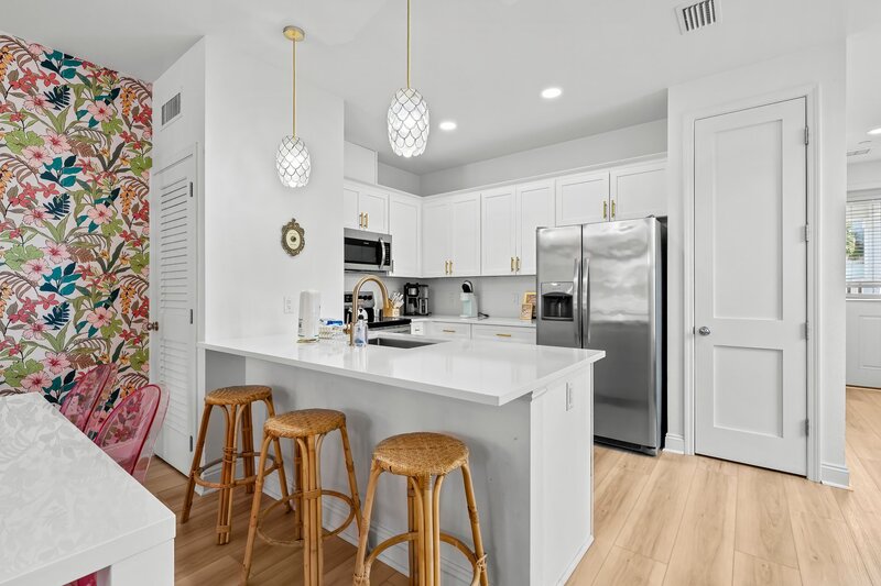 White modern kitchen with island seating, stainless steel appliances, and tropical flair—ideal for families and groups vacationing near Alys Beach and 30A.