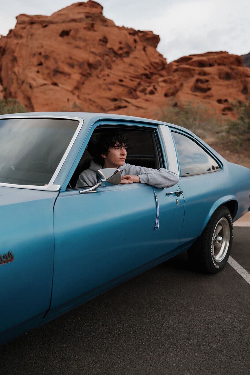 The guy is sitting in a car parked on the desert road, looking out of the window