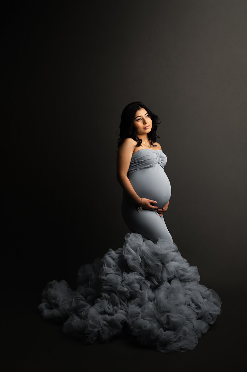 Pregnant mother in tight grey dress holding her baby bump looking up at the light